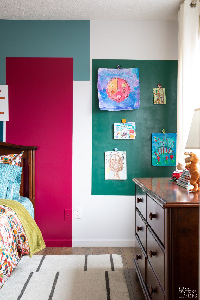غرفة نوم طفل معتم بالألوان مع فن معلق على الحائط.