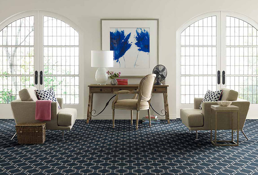 غرفة معيشة ببابين فرنسيين كبيرين ، مزينة بأرائك بنية اللون ، ودراسة خشبية ، وكرسي على سجادة منقوشة باللونين الأزرق والأبيض.