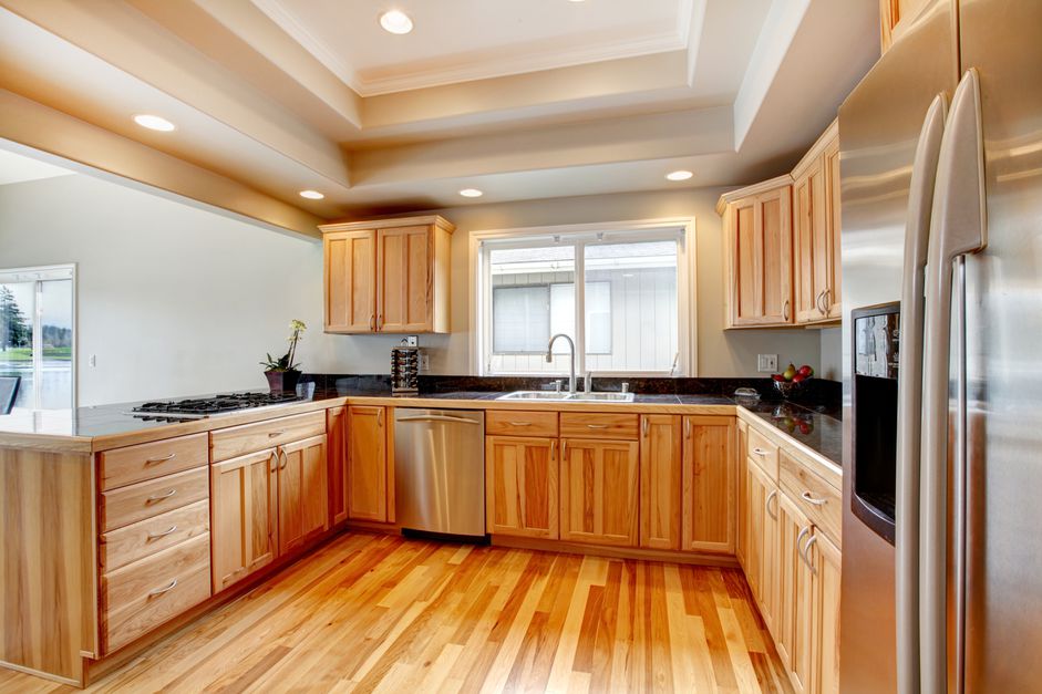 مطبخ خشبي مع أسطح منضدة سوداء وأرضية خشبية وسقف مجوف أبيض