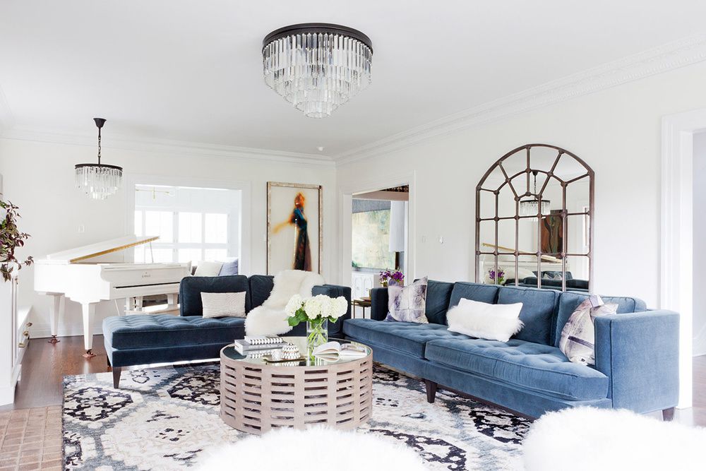 صوفا مخملية زرقاء وأريكة في غرفة المعيشة مع بيانو أبيض ومرآة حائط كبيرة مقوسة